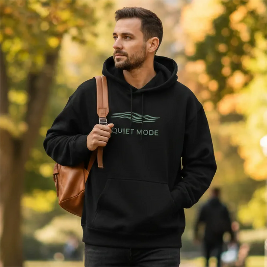 Man wearing a black hoodie with 'The Quiet Mode' logo, holding a brown bag in a park setting.